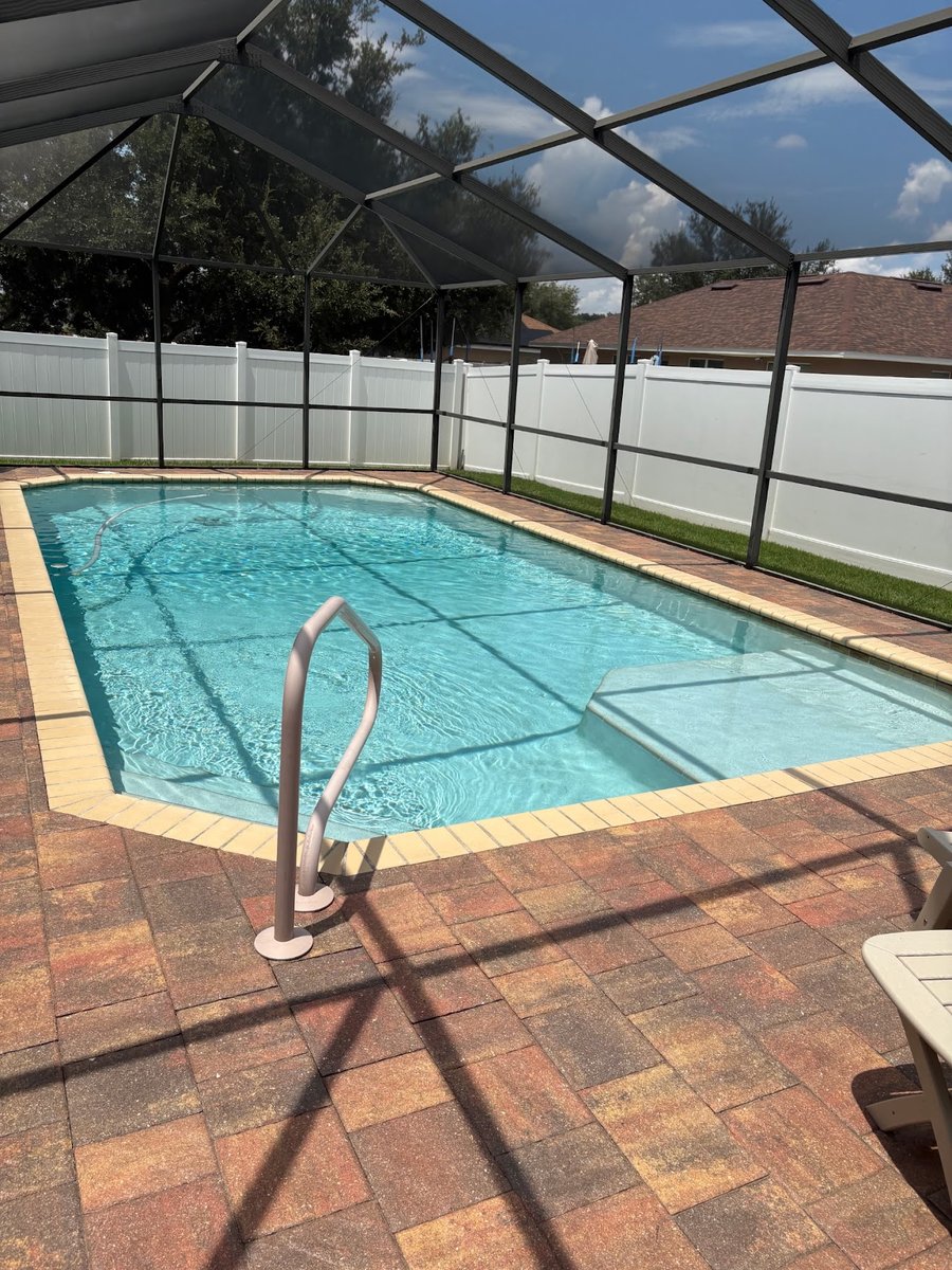 Crystal-clear client pool under a screened lanai with brick paver deck